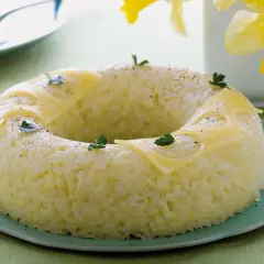 Sformato di riso a ciambella, decorato con fette di formaggio e prezzemolo, su un piatto verde.