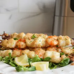 Spiedini di gamberi e calamari impanati, cotti alla perfezione nella friggitrice ad aria. Serviti su un letto di insalata con spicchi di limone.