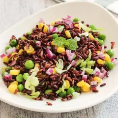 Insalata di riso Venere colorata con piselli, mais, cipolla rossa e lattuga croccante, guarnita con menta fresca.