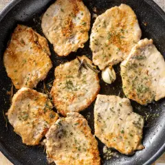 Fette di lonza di maiale in padella, dorate e morbide, condite con erbe aromatiche e aglio.