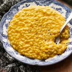 Un cremoso risotto alla zucca, cosparso di pepe nero, servito su un piatto decorato con un motivo floreale blu.