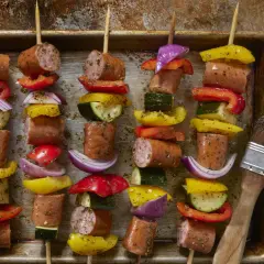 Spiedini di carne succulenta alternati a peperoni colorati, cipolla rossa e zucchine, pronti per essere grigliati.
