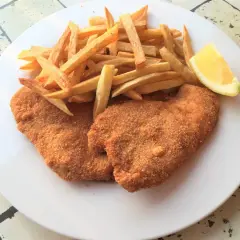 Due cotolette di pollo dorate e croccanti, accompagnate da patatine fritte e uno spicchio di limone su un piatto bianco.