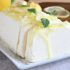 Un delizioso semifreddo al limone, guarnito con scorzette, menta e una glassa gialla, pronto per essere gustato.