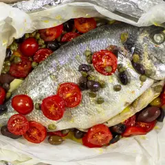 Orata al cartoccio con pomodorini, olive e capperi, un piatto profumato e saporito pronto per essere gustato.