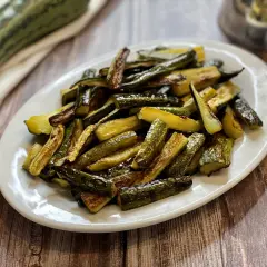 Zucchine al forno con pangrattato e parmigiano, dorate e croccanti, servite su un piatto bianco.