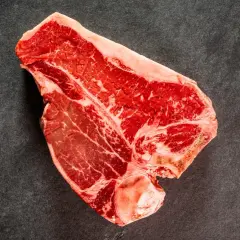 Una succulenta bistecca di manzo T-bone, con la sua marmorizzazione di grasso, pronta per essere cucinata su una superficie scura.