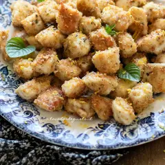 Bocconcini di pollo dorati e croccanti, guarniti con scorza di limone e foglie di menta fresca, serviti su un piatto decorato.