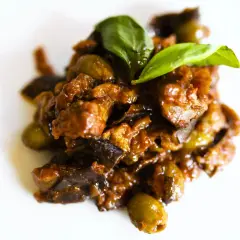 Un saporito piatto di caponata di pesce spada, con melanzane, olive e basilico fresco, pronto per essere gustato.