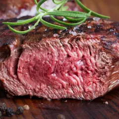 Succulenta tagliata di manzo al sangue, guarnita con rosmarino fresco e grani di pepe su un tagliere di legno.