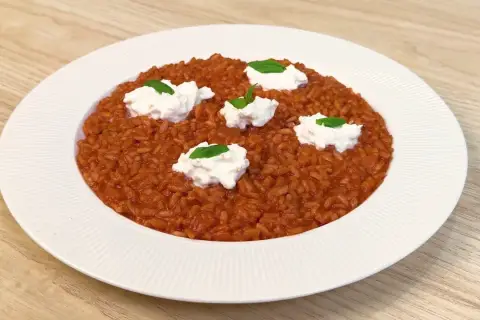 Un invitante risotto al pomodoro, arricchito da ciuffi di ricotta fresca e basilico, pronto per essere gustato.