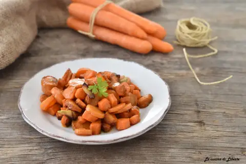 Carote in padella, dolci e caramellate, guarnite con prezzemolo fresco su un piatto bianco. Sullo sfondo, carote fresche legate con spago.