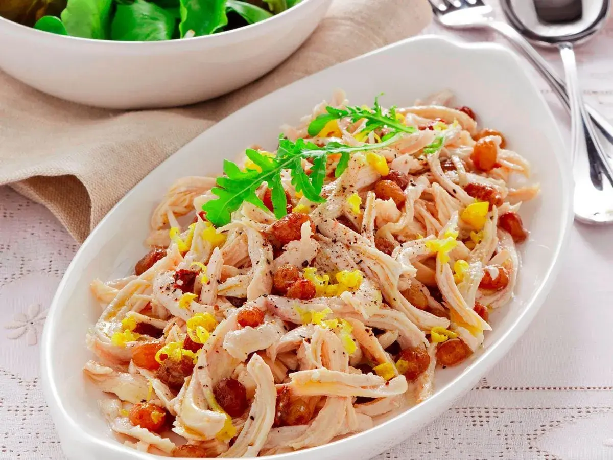 Insalata di pollo sfiziosa con uvetta e scorza di limone, guarnita con rucola fresca.