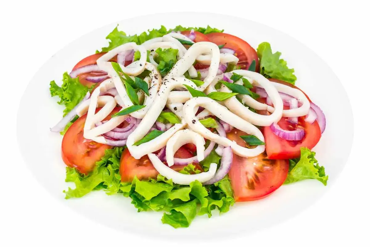 Deliziosa insalata di calamari con pomodori, cipolla rossa e lattuga fresca, condita con erbe aromatiche.