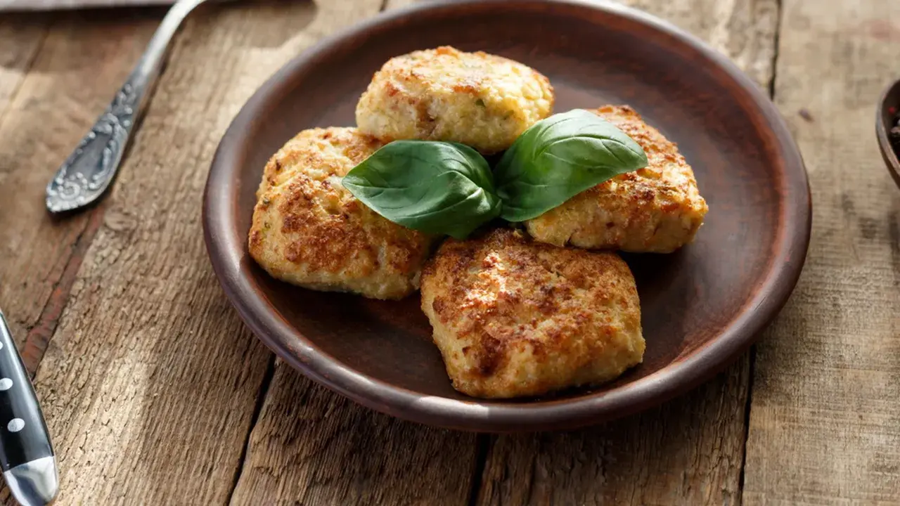 Quattro polpette di zucchine e patate dorate, guarnite con basilico fresco, su un piatto di terracotta.