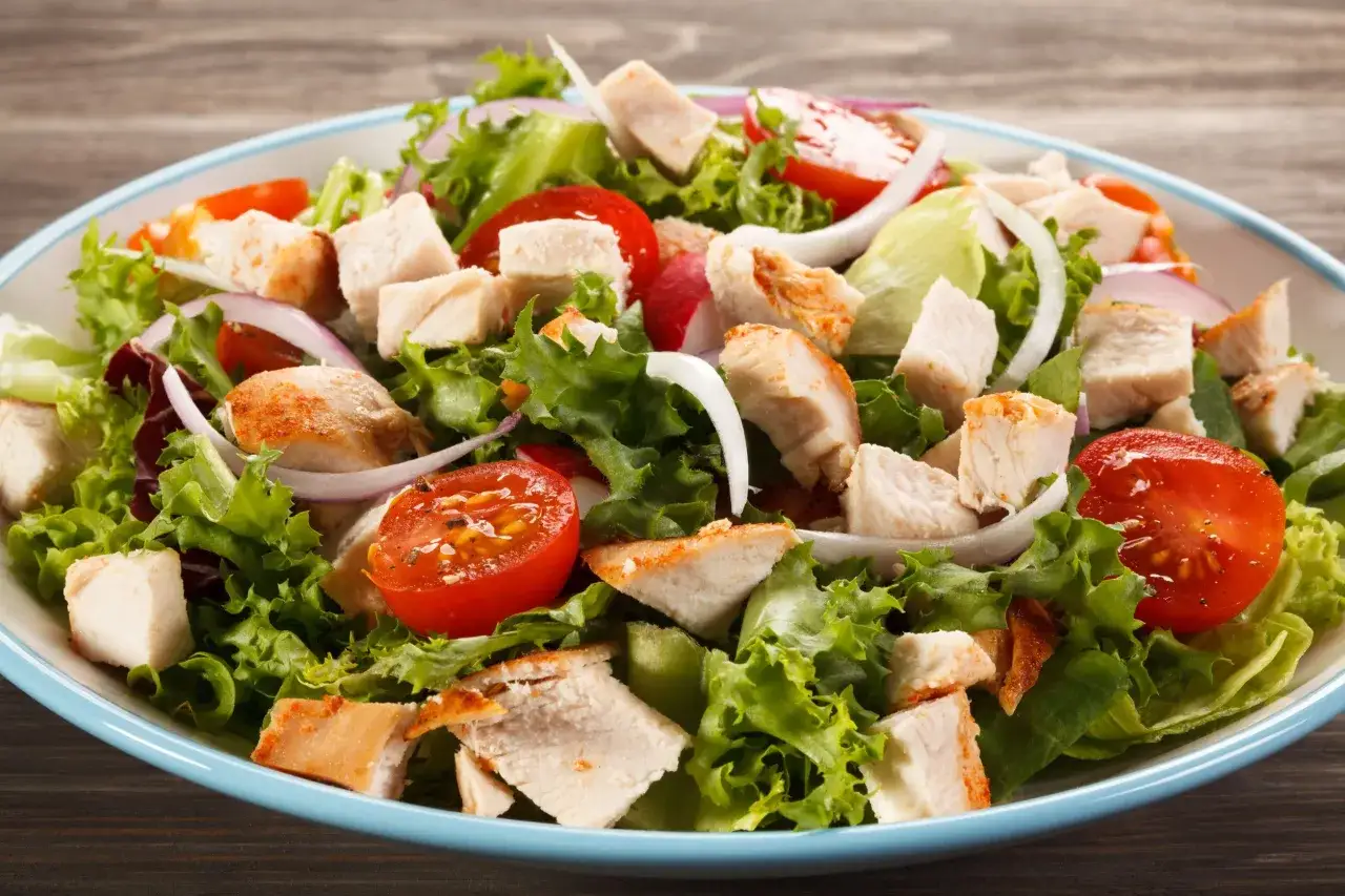 Insalata di pollo fredda con lattuga croccante, pomodorini succosi, cipolla rossa e pezzi di pollo grigliato.
