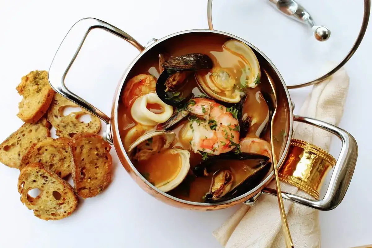 Un invitante brodetto di pesce in una pentola di rame, con crostini croccanti e un cucchiaio dorato.
