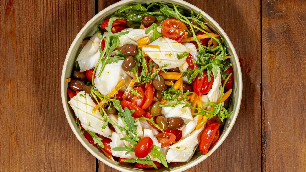 Insalata di calamari fresca con pomodorini, olive, rucola e carote julienne, un piatto leggero e saporito.