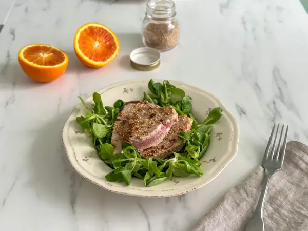 Tonno in padella con crosta di sesamo su letto di insalata fresca, accompagnato da spicchi d'arancia.
