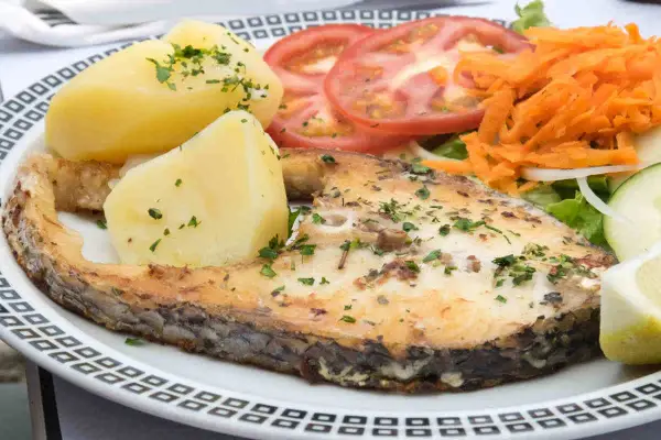 Un succulento pesce spada al forno, servito con patate bollite, pomodori a fette, carote grattugiate e insalata fresca.